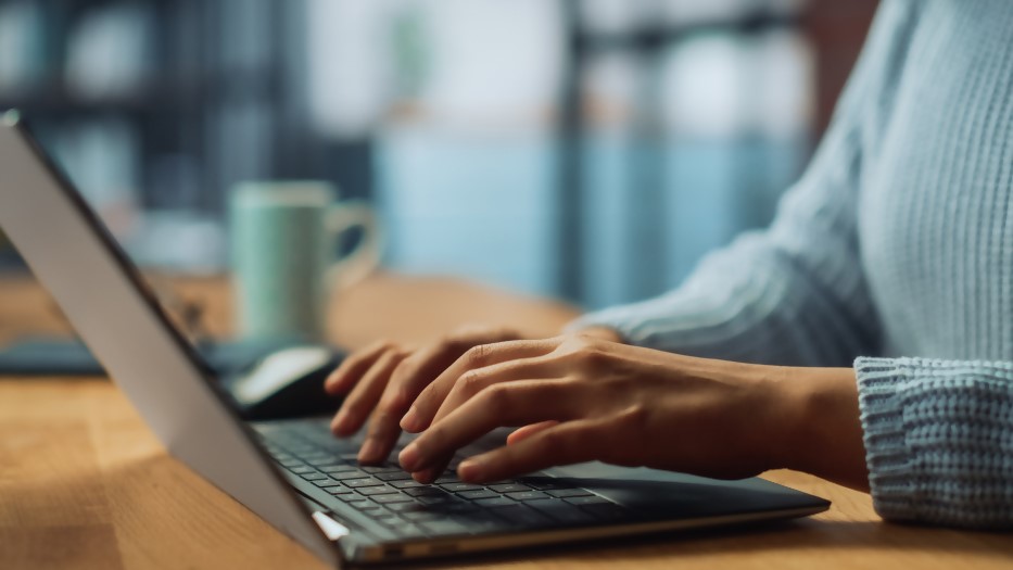 Eine Frau schreibt auf der Tastatur eines Laptops. Der Bildfokus liegt auf ihren Händen.