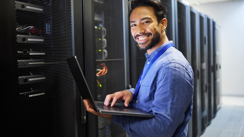 Ein IT-Mitarbeiter prüft mit einem Laptop in einem Serverraum die Technik. 
