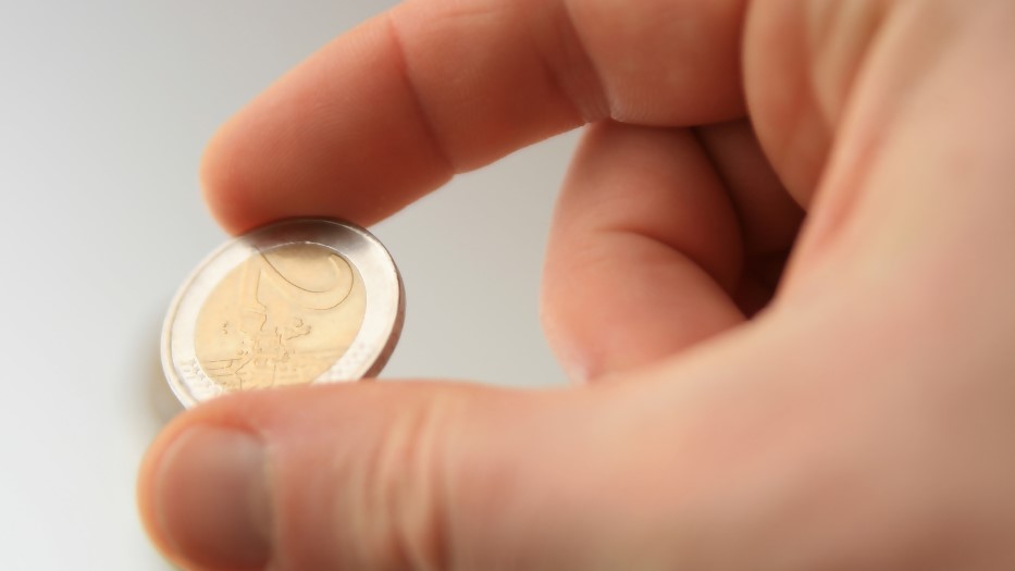 Eine rechte Hand hält eine 2-Euro-Münze zwischen Daumen und Zeigefinger.
